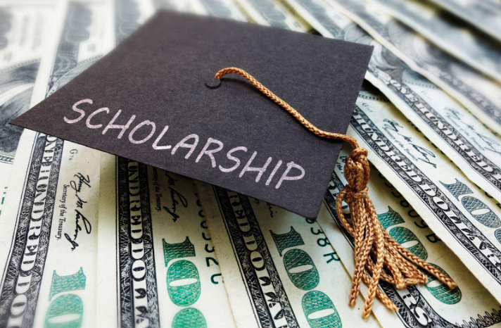 image of a graduation cap with the word "scholarship" written on it. the background is dollar bills